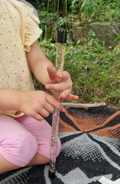 Kind hält Zauberstab in der Hand gefüllt mit Wasser und Glitzer